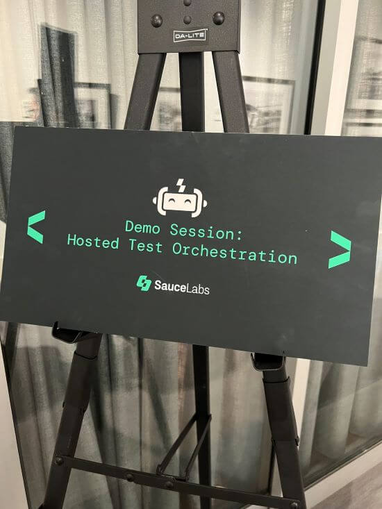 A photograph of a sign with text that reads: "Demo Session: Hosted Test Orchestration."
